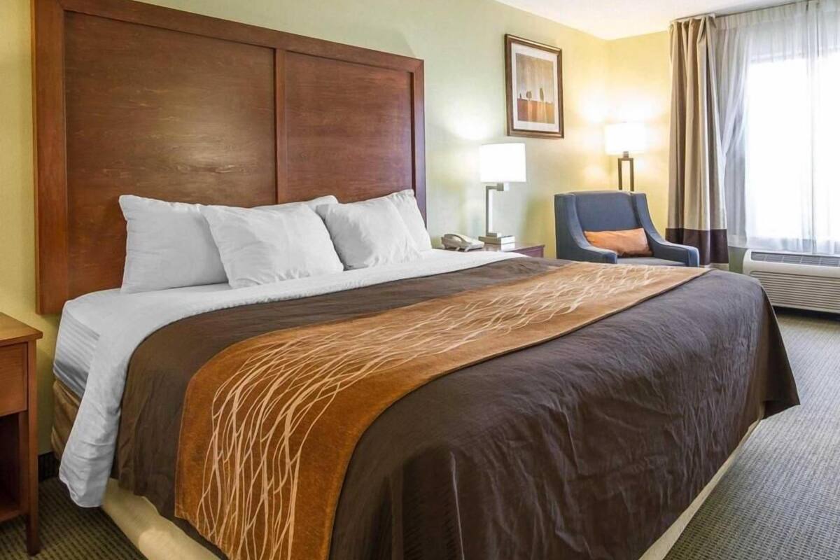 A hotel room with a large bed, a chair, a desk, and a window with curtains.
