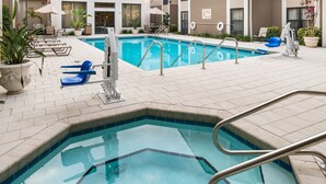 A swimming pool with a tiled deck, lounge chairs, and potted plants.
