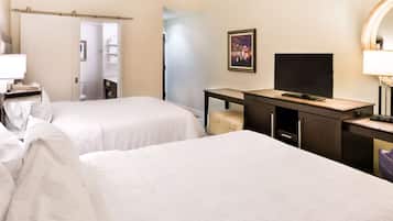 A hotel room with two beds, a desk with a television, a mirror, and a bathroom visible through an open door.