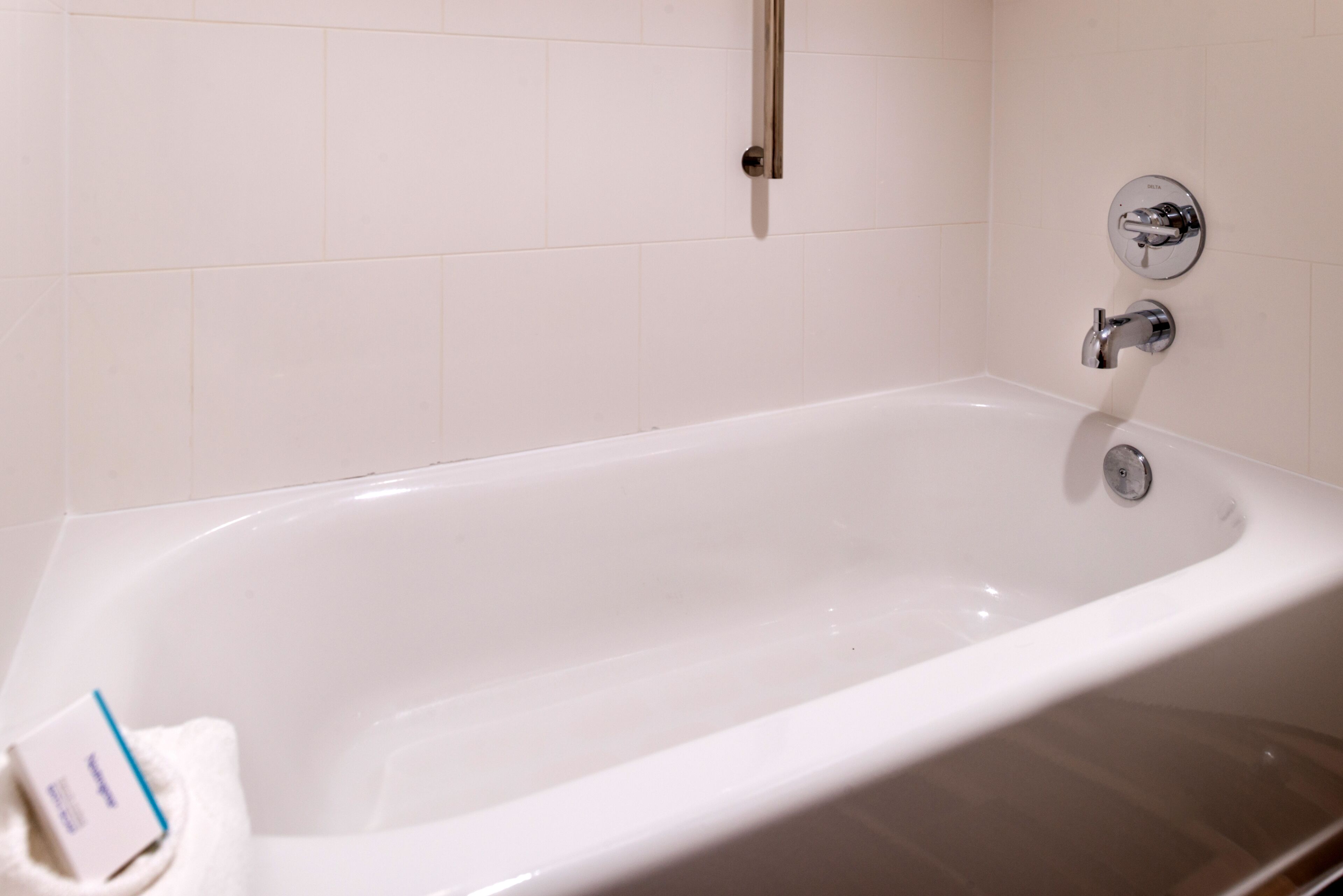 A white bathtub with chrome fixtures, a white towel, and a white tiled wall.