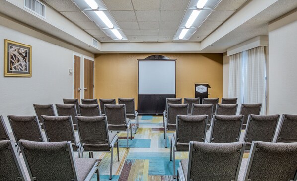 A conference room with rows of chairs facing a projection screen, a podium, and a framed picture on the wall.