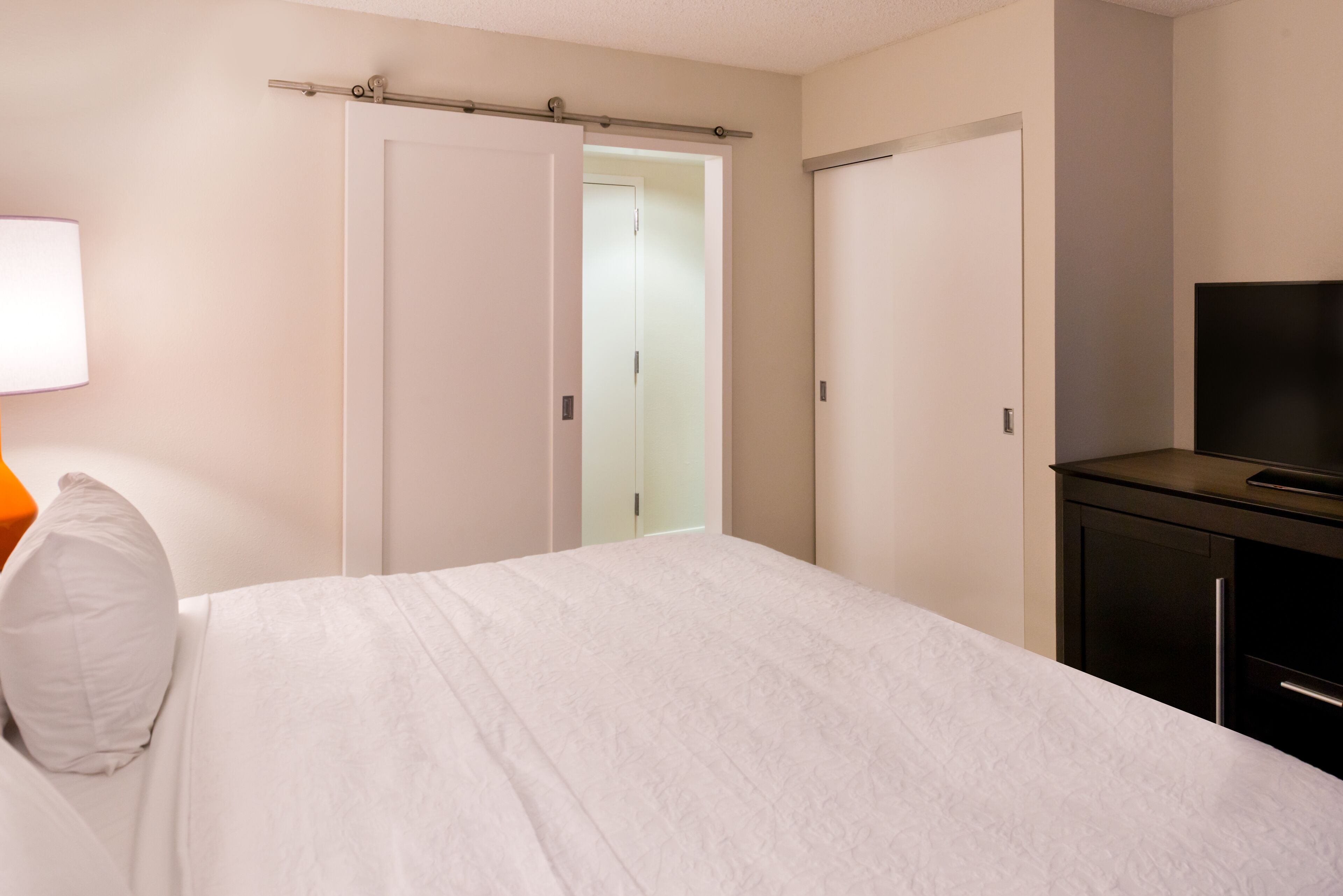 Une chambre à coucher comprenant un lit, une table de chevet, une lampe, un téléviseur et une armoire.