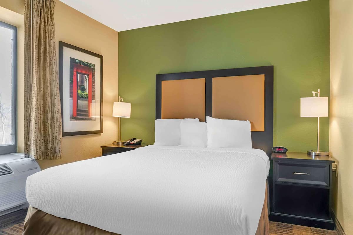Habitación de hotel con una cama grande, dos mesitas de noche, una ventana con cortinas e imagen enmarcada en la pared.