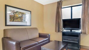 Een woonkamer met een bruine leren bank, een bijzettafeltje, een flatscreen televisie op een zwart voetstuk en een lijst met een foto aan de muur.