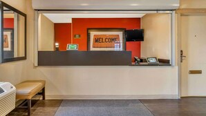 Een receptiegedeelte met een 'WELCOME'-bord, een bureau met een computer, telefoon en een bank.