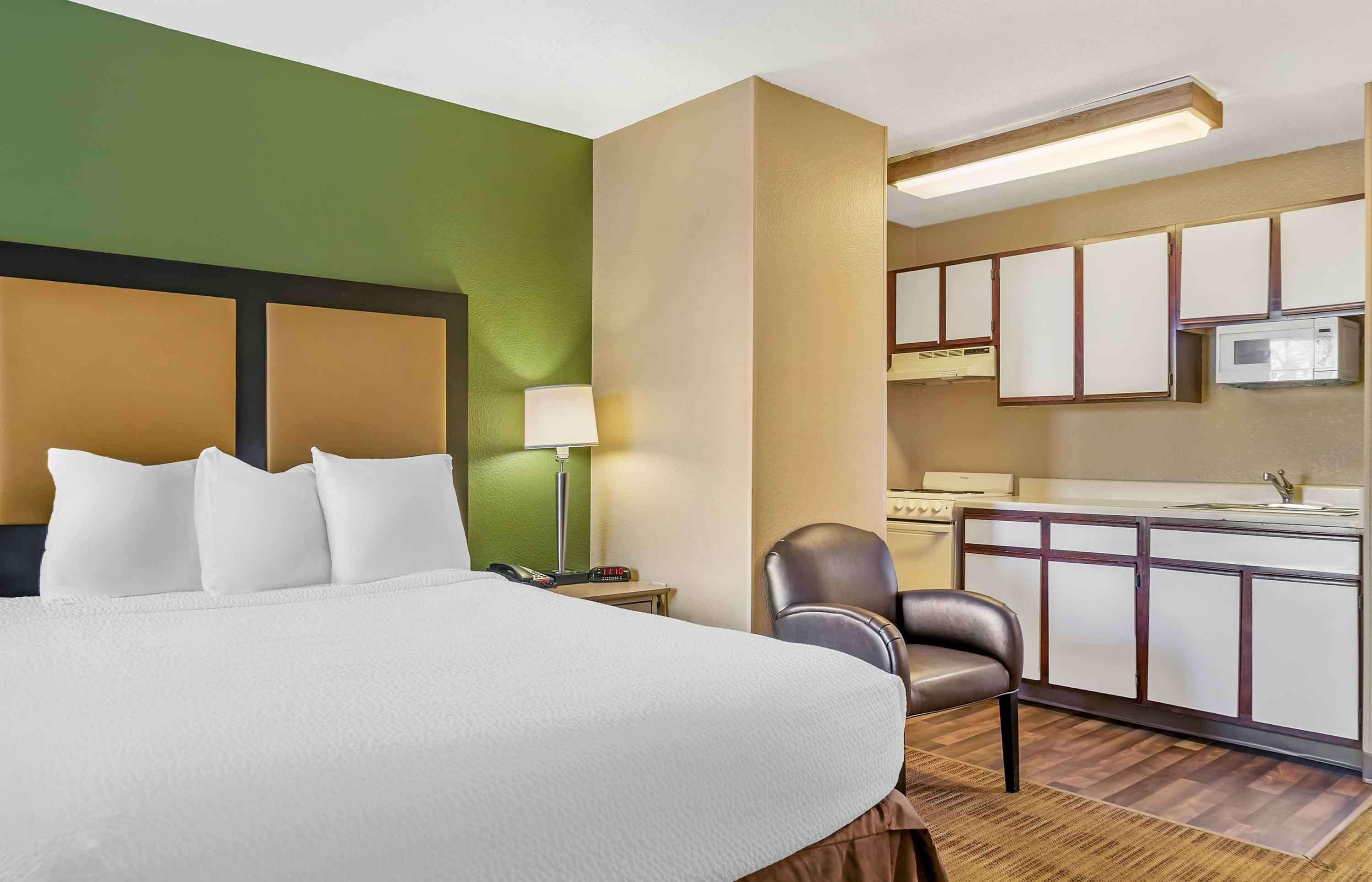 A hotel room with a large bed, a desk with a chair, a microwave, and a kitchenette.
