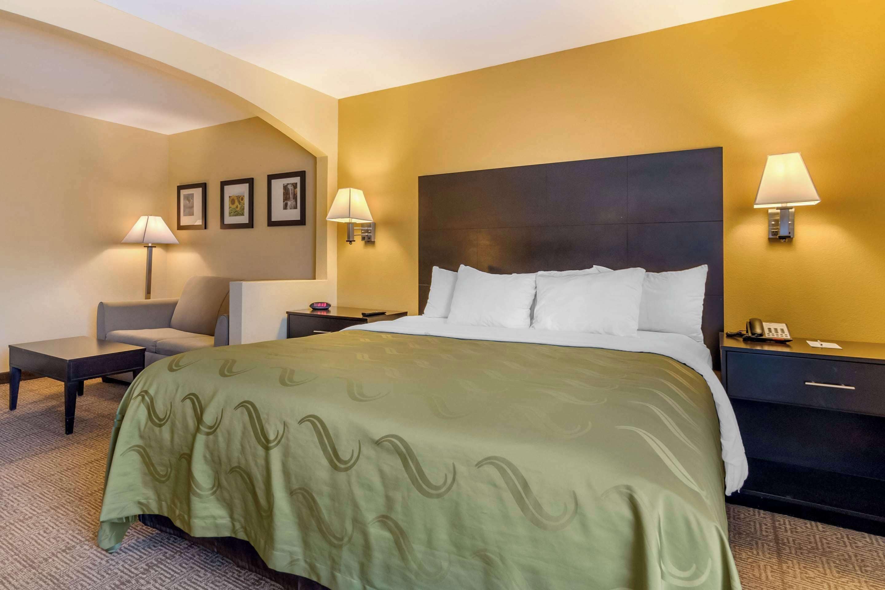 Une chambre d’hôtel avec un grand lit, deux tables de chevet, une chaise et des lampes fixées au mur.