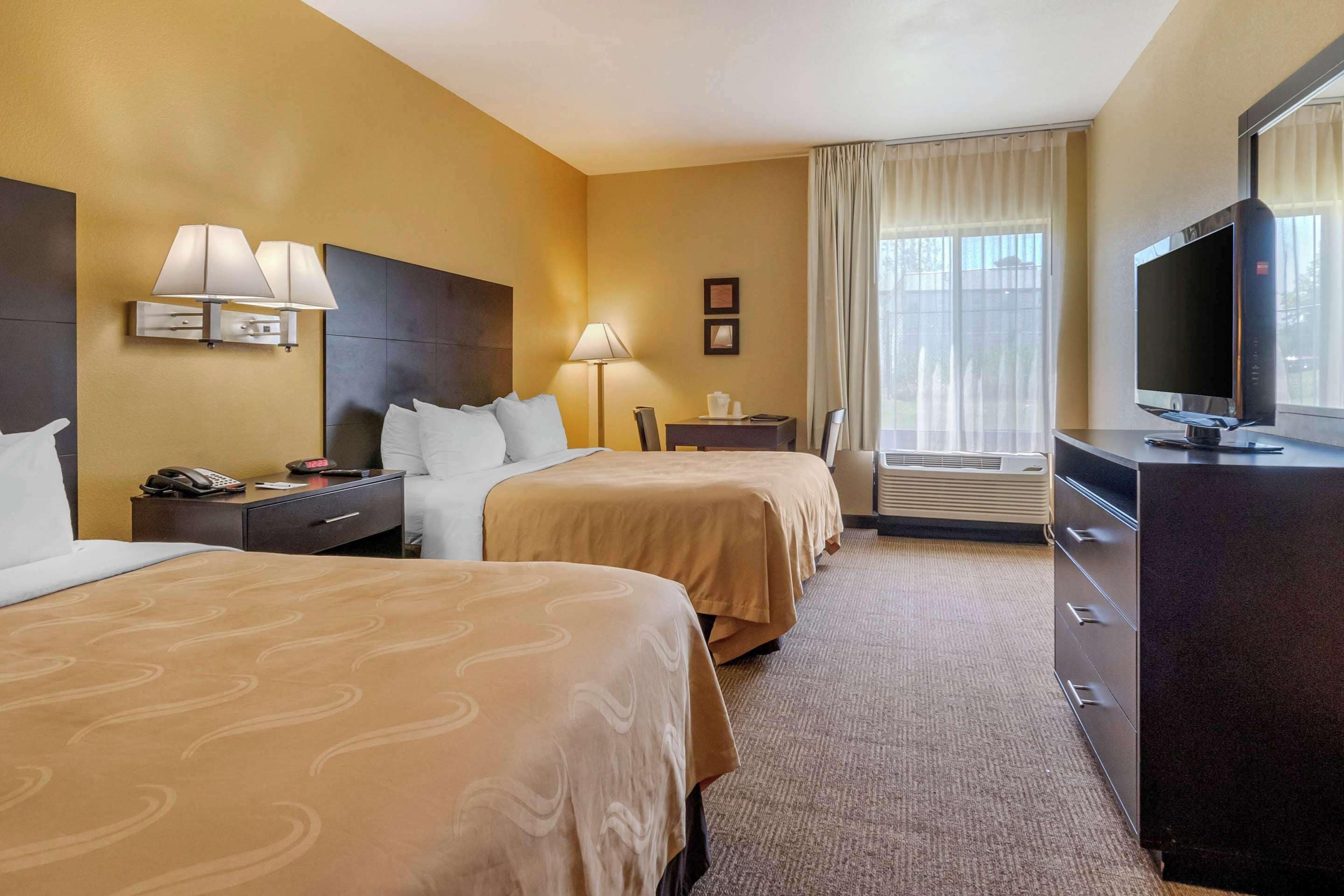 Une chambre d’hôtel avec deux lits, un bureau, une télévision et une fenêtre avec des rideaux.