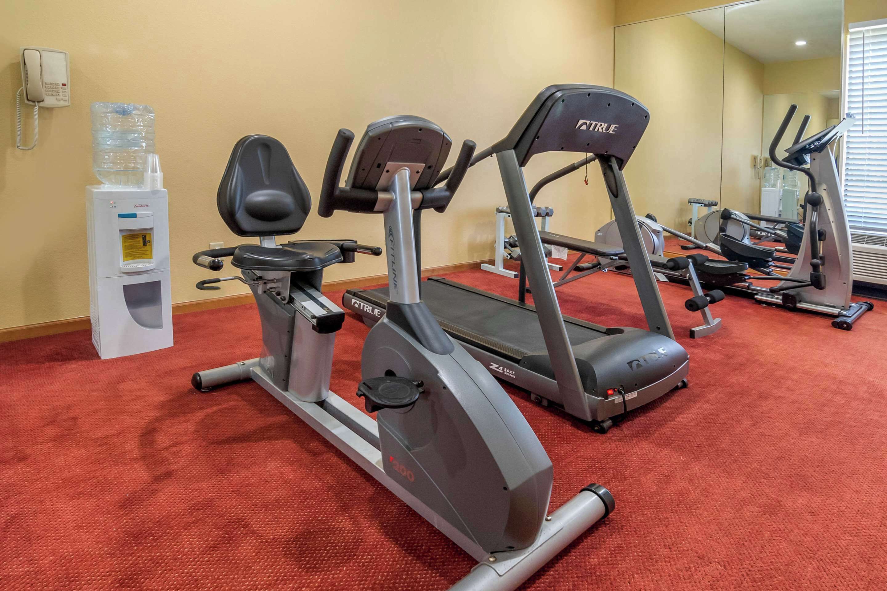 Un gimnasio con cintas de correr, bicicletas estáticas y un dispensador de agua.