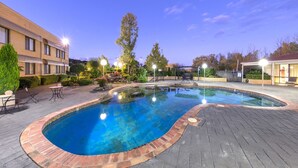 A swimming pool with a brick border, surrounded by a patio area with outdoor furniture and a building in the background. - Garden City Hotel, BW Signature Collection (Narrabundah)