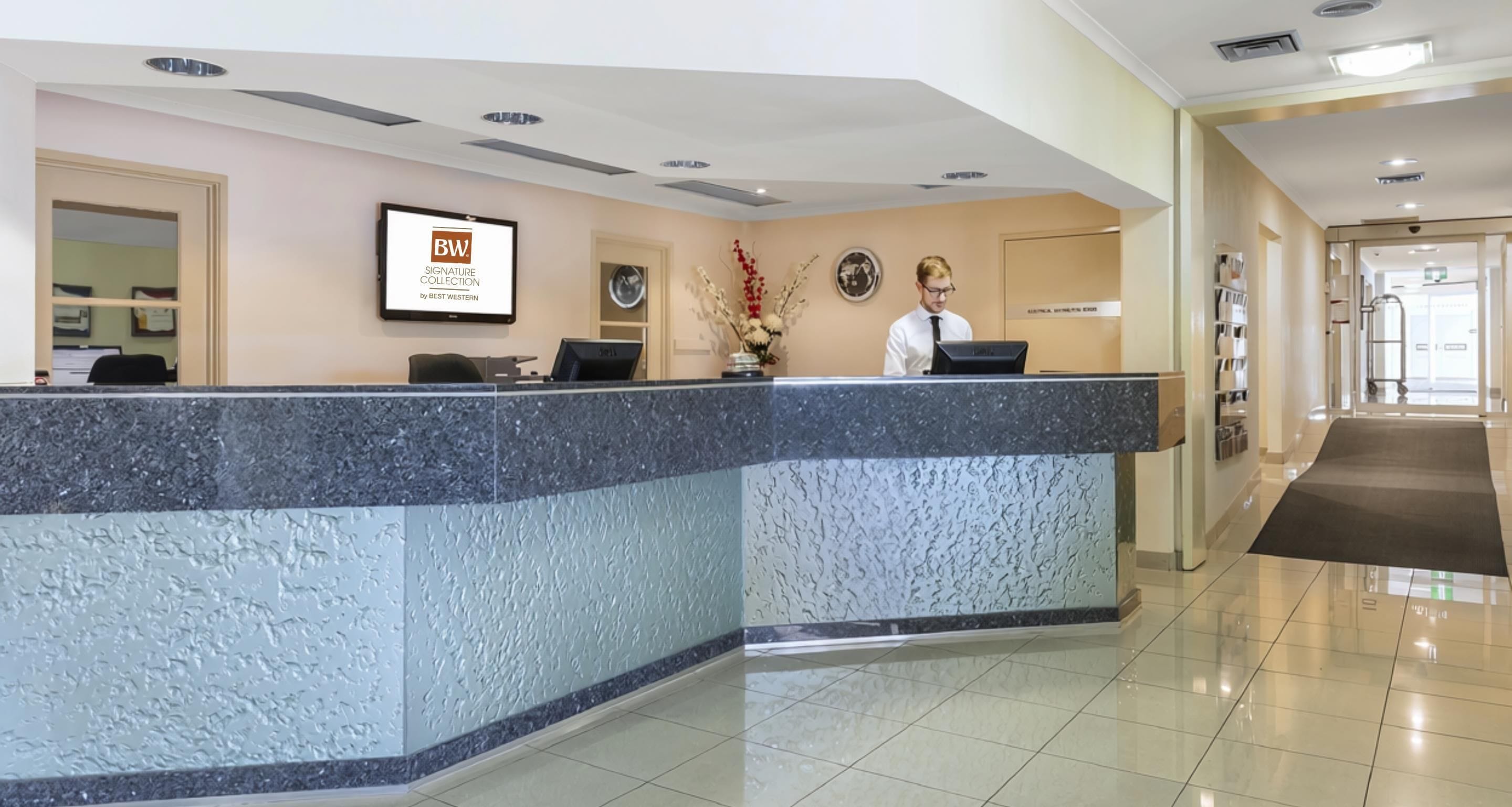 Una reception hotel con un bancone in marmo, una targa incorniciata e un receptionist.