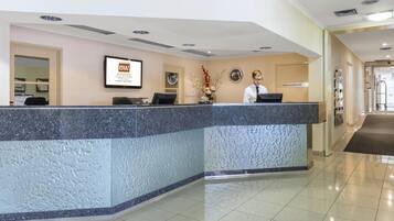 Uma área de recepção de hotel com balcão de mármore, uma placa emoldurada e um recepcionista.