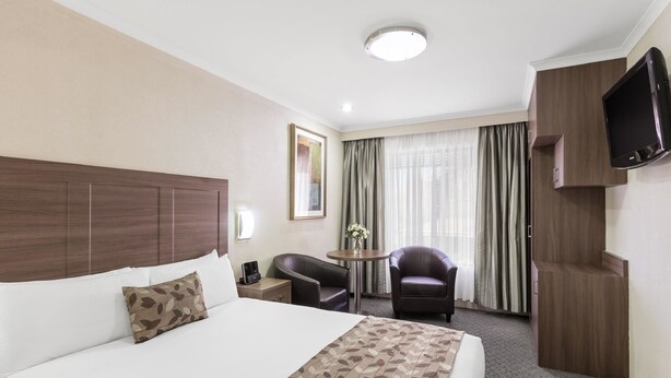 A hotel room with a large bed, a desk, a chair, a TV, and a window with curtains. - Garden City Hotel, BW Signature Collection (Narrabundah)