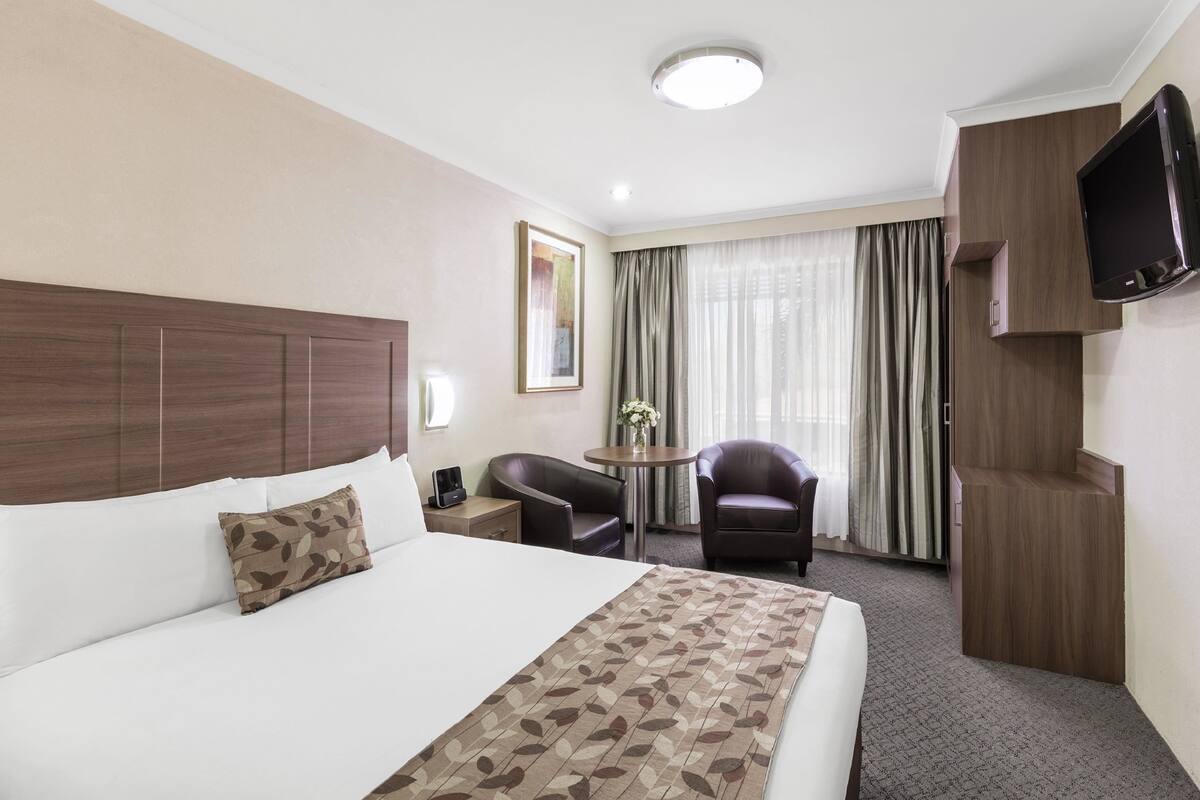 A hotel room with a large bed, a desk, a chair, a TV, and a window with curtains.