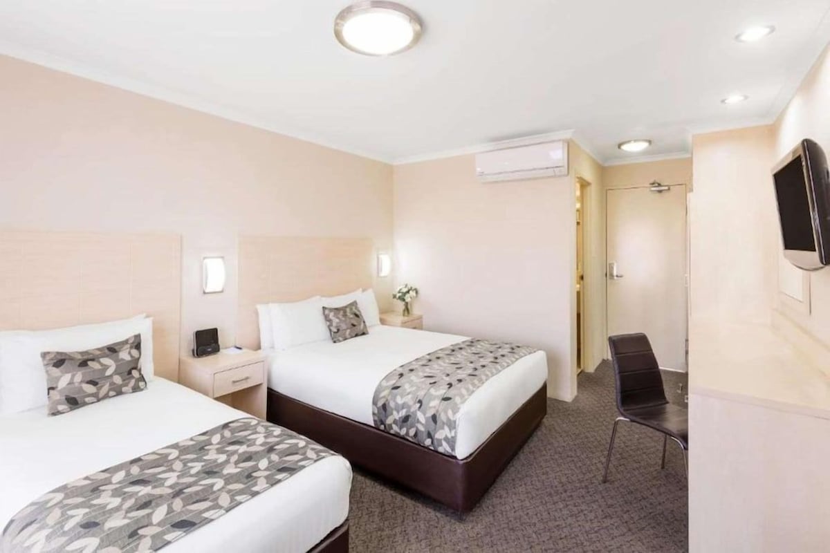 Une chambre d’hôtel avec deux lits, un bureau, une chaise, un appareil de climatisation et un téléviseur.