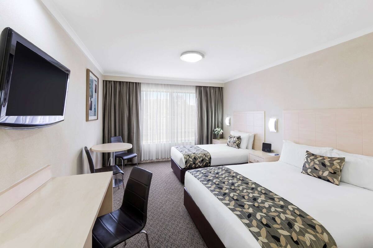 A hotel room with two beds, a TV, a desk, and a chair.