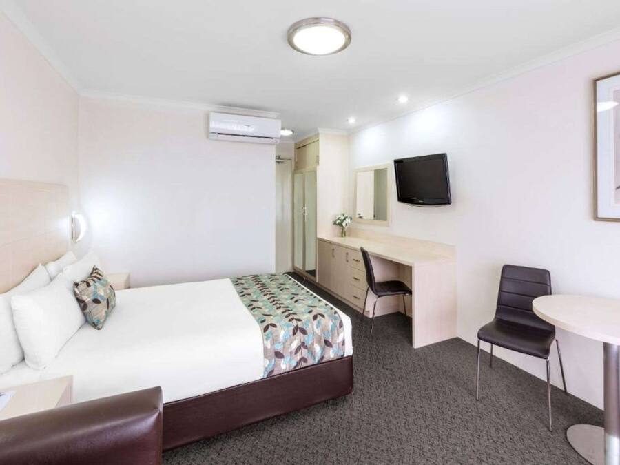Ein Hotelzimmer mit Bett, Schreibtisch, Stuhl, Fernseher und Klimaanlage.
