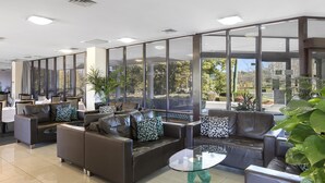 A modern lobby with leather sofas, a glass coffee table, and large windows offering a view of the outdoors. - Garden City Hotel, BW Signature Collection (Narrabundah)