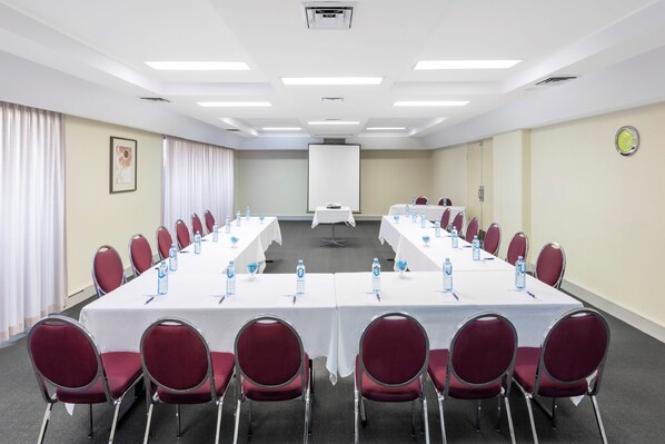 A conference room with a long table, red chairs, water bottles, and a projector screen. - Garden City Hotel, BW Signature Collection (Narrabundah)
