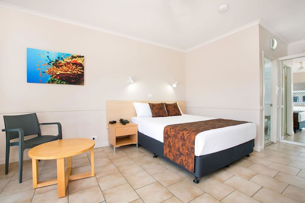 A hotel room with a bed, bedside table, chair, and a painting on the wall.