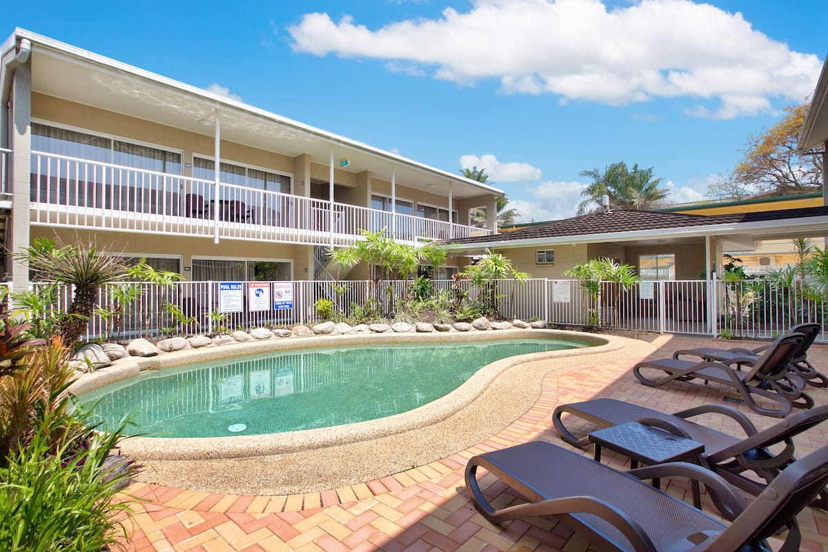 A hotel with a swimming pool, lounge chairs, and a fenced area with plants.