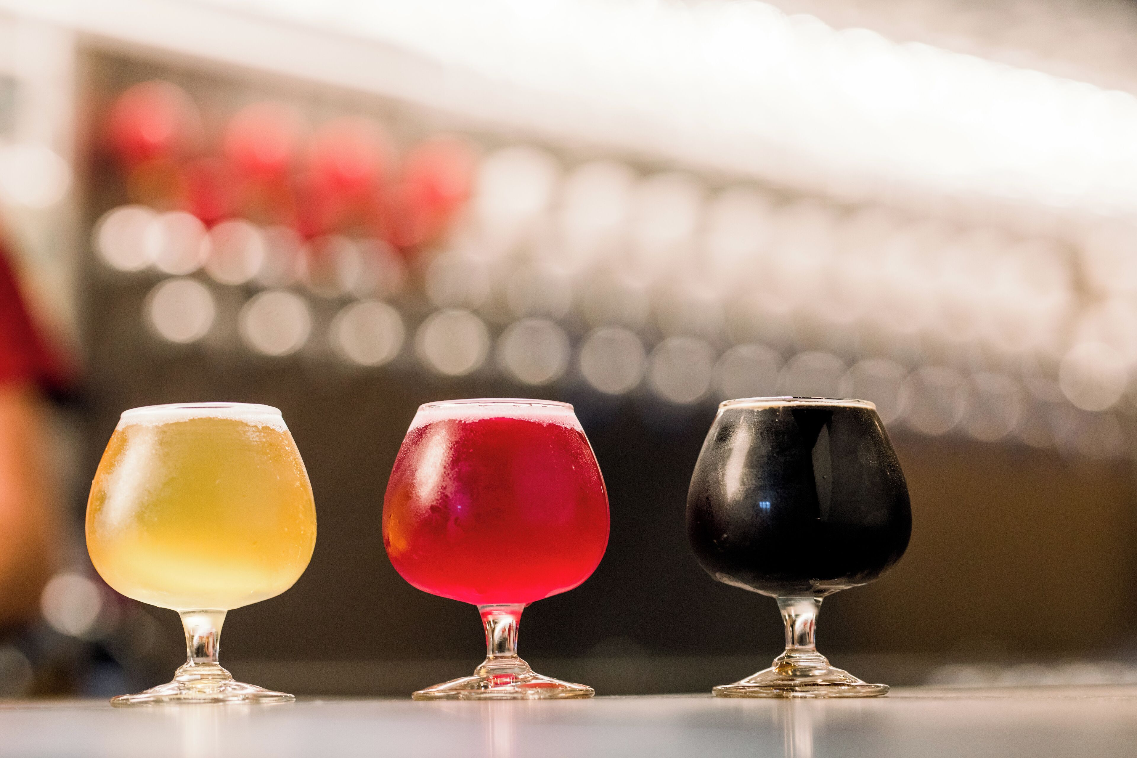 Three glasses of different colored beverages on a bar counter.