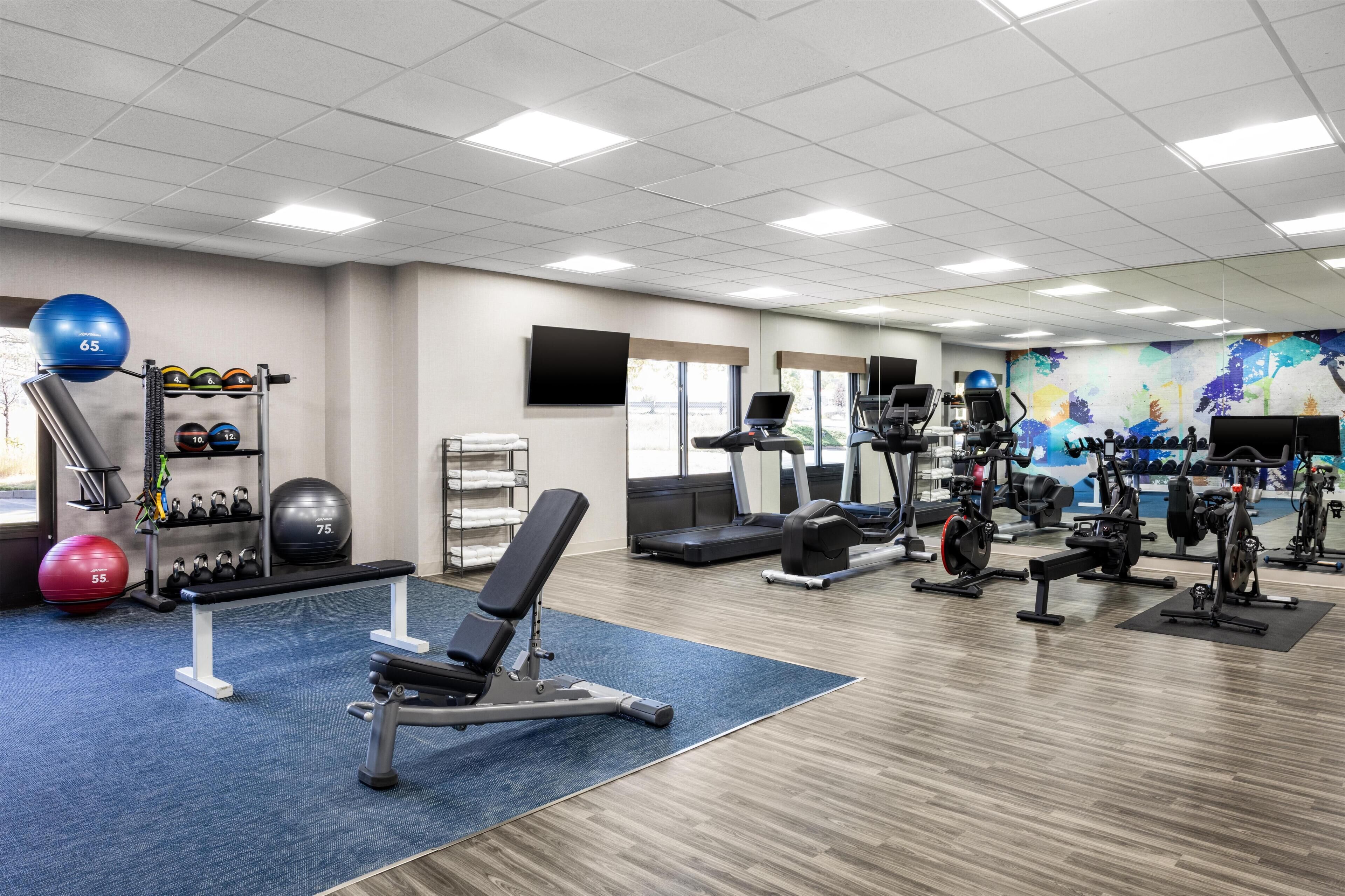 A gym with exercise equipment, a bench, and a wall-mounted TV.