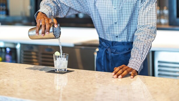A bartender pouring a drink into a glass.