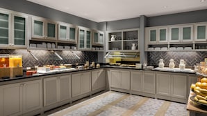 A modern kitchen with grey cabinets, a herringbone tile backsplash, and a buffet setup.