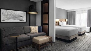 A hotel room with a sofa, a small table, a bed, and a large window with curtains.