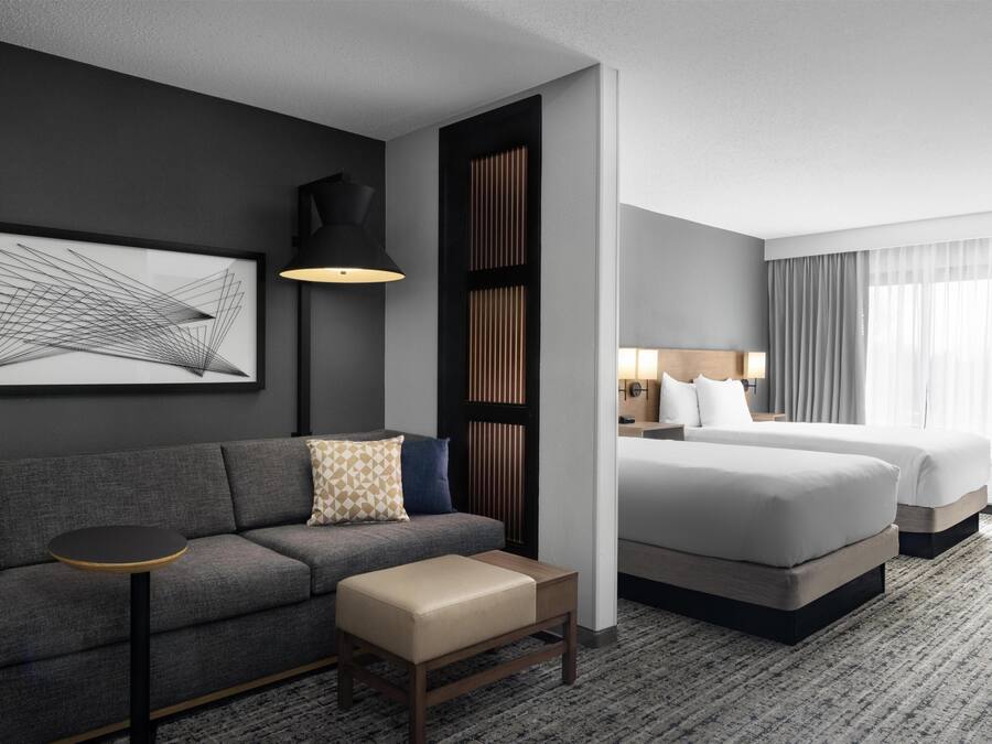 A hotel room with a sofa, a small table, a bed, and a large window with curtains.