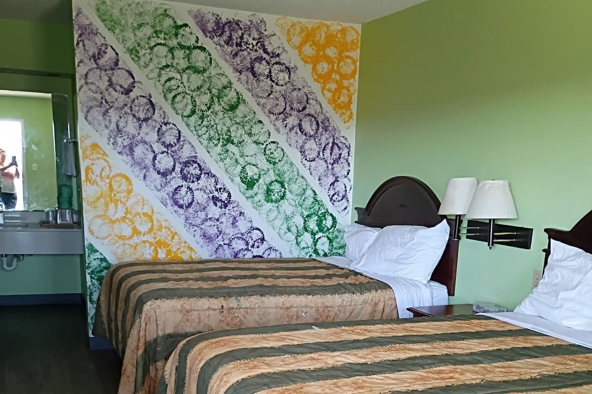 A hotel room with two beds, a green wall, and a floral tapestry.