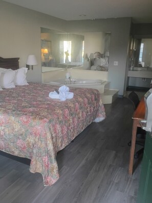 A hotel room with a bed, a desk, a chair, a bathroom with a sink and mirror, and a large mirror on the wall.