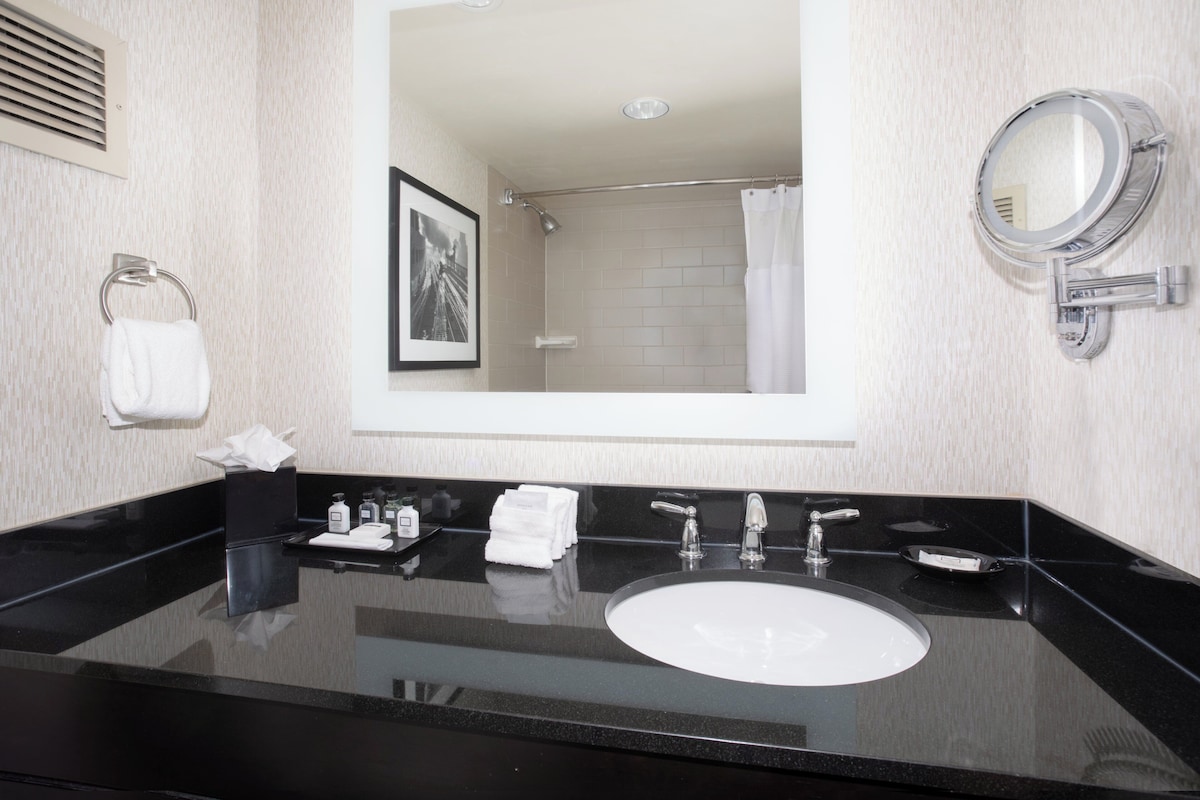 Un baño moderno con un lavabo negro, un espejo, un perchero y un cuadro enmarcado en la pared.
