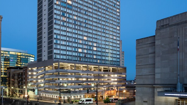 Un hotel de gran altura con diseño moderno, destacando un letrero grande en la parte superior y una estructura de estacionamiento de varios niveles abajo.