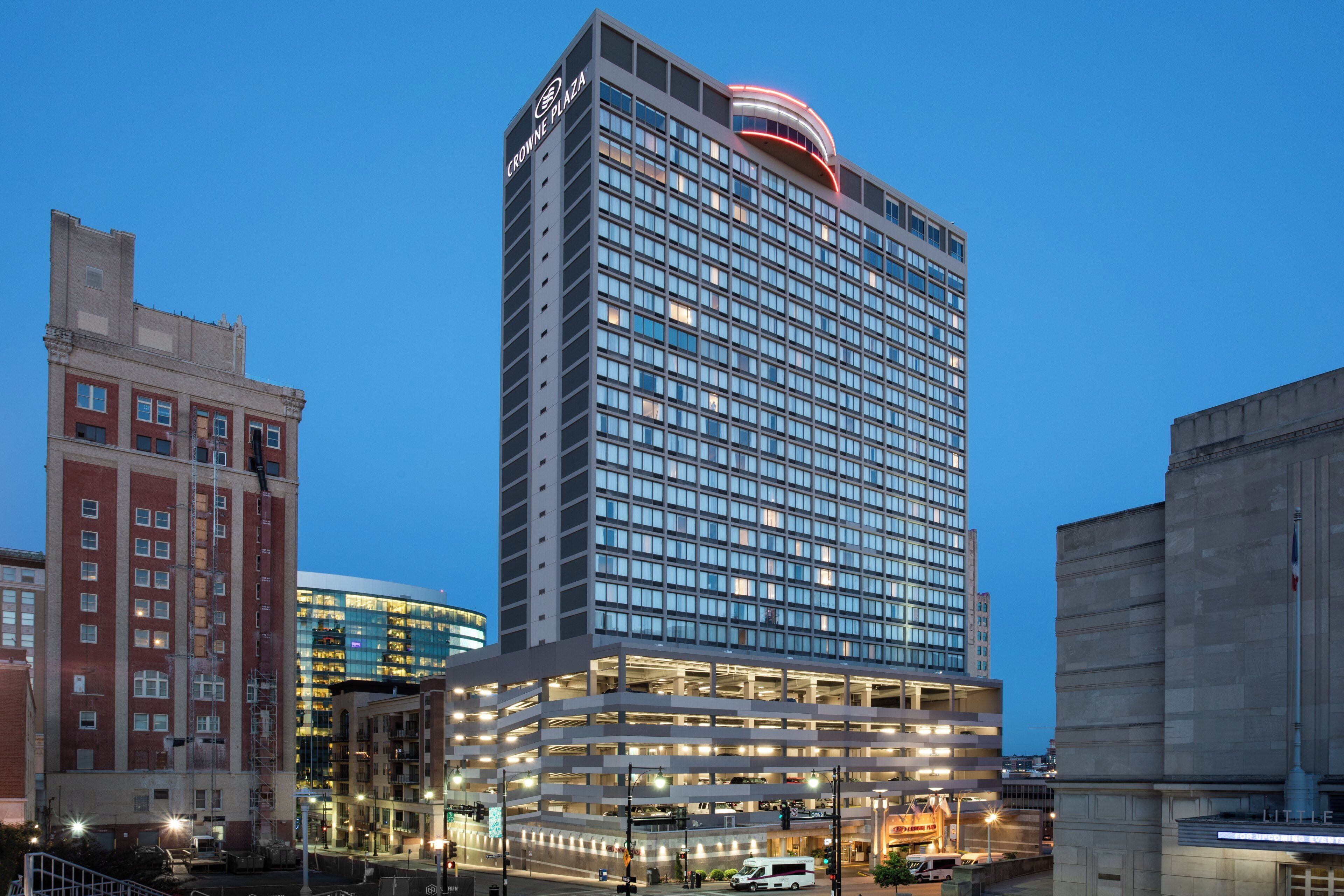 A multi-story hotel with a prominent sign at the top, a parking garage below, and a mix of older and modern buildings in the vicinity.