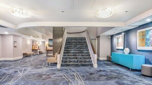A hotel lobby with a grand staircase, a blue reception desk, and a patterned carpet. - Crowne Plaza Kansas City Downtown by IHG (Kansas City)