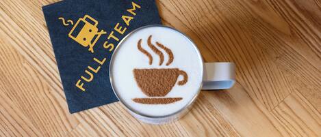 A cup of coffee with a steam design, a napkin with 'FULL STEAM' text, and a wooden table.