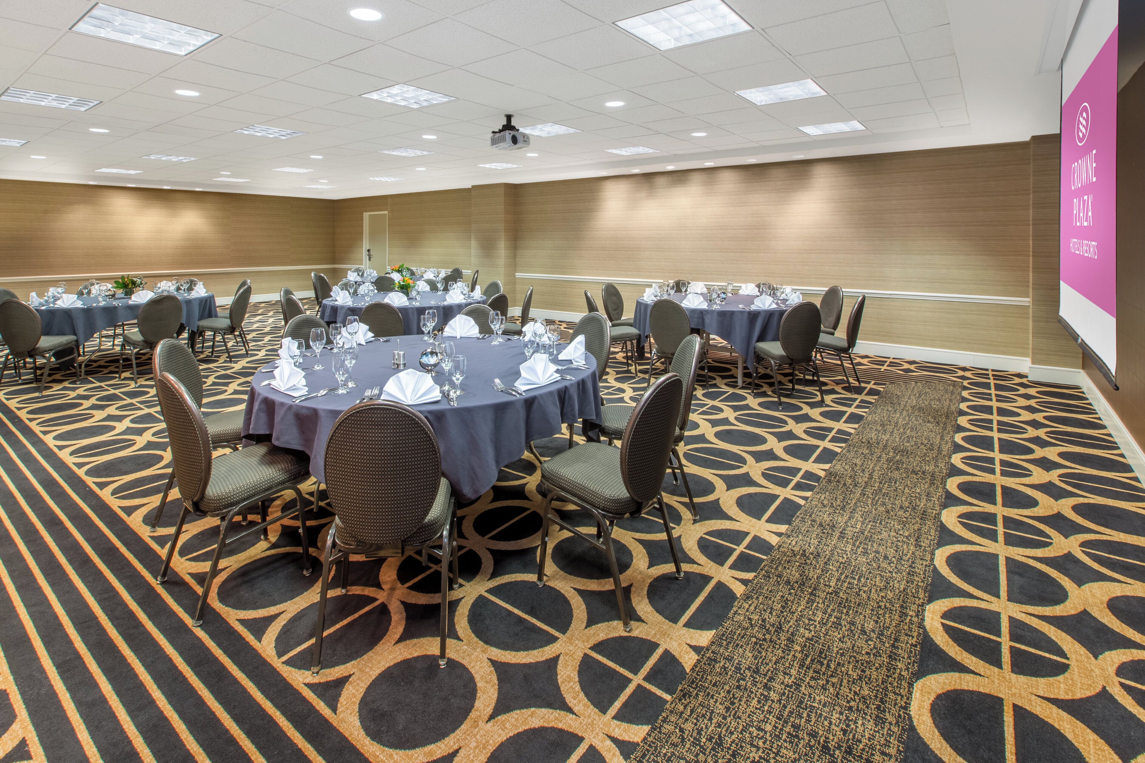 A conference room with round tables, chairs, and a carpeted floor.