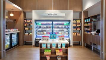 Et moderne butiksareal med en central udstilling af snacks og drikkevarer, omgivet af reoler fyldt med forskellige produkter.
