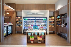 Un espacio comercial moderno con un expositor central de aperitivos y bebidas, rodeado de estanterías llenas de diversos productos.