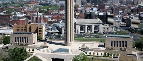 A cityscape with a prominent monument in the foreground, surrounded by green spaces and a mix of modern and historic buildings in the background.