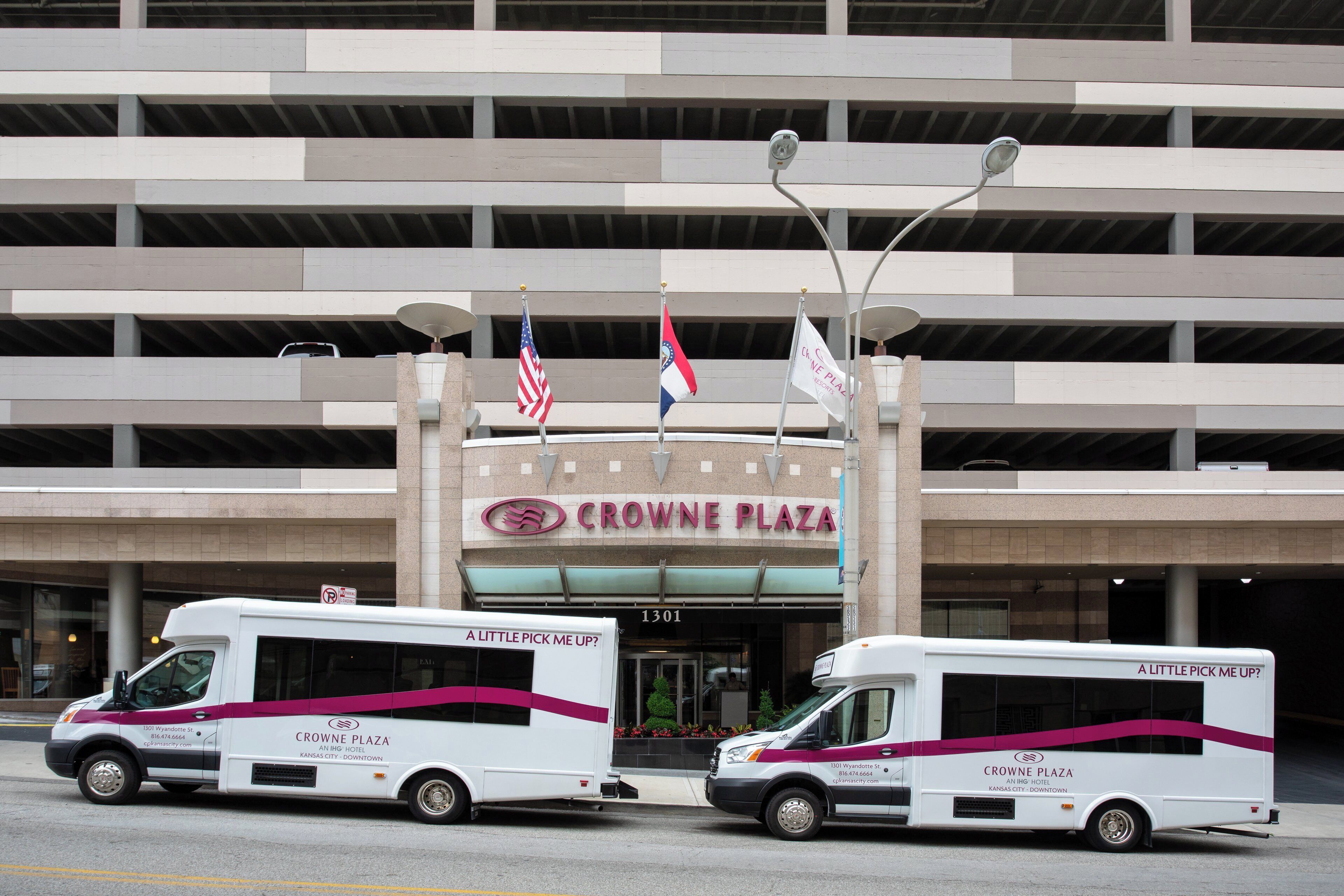 A building with a sign reading 'CROWNE PLAZA' and two shuttle buses parked in front.