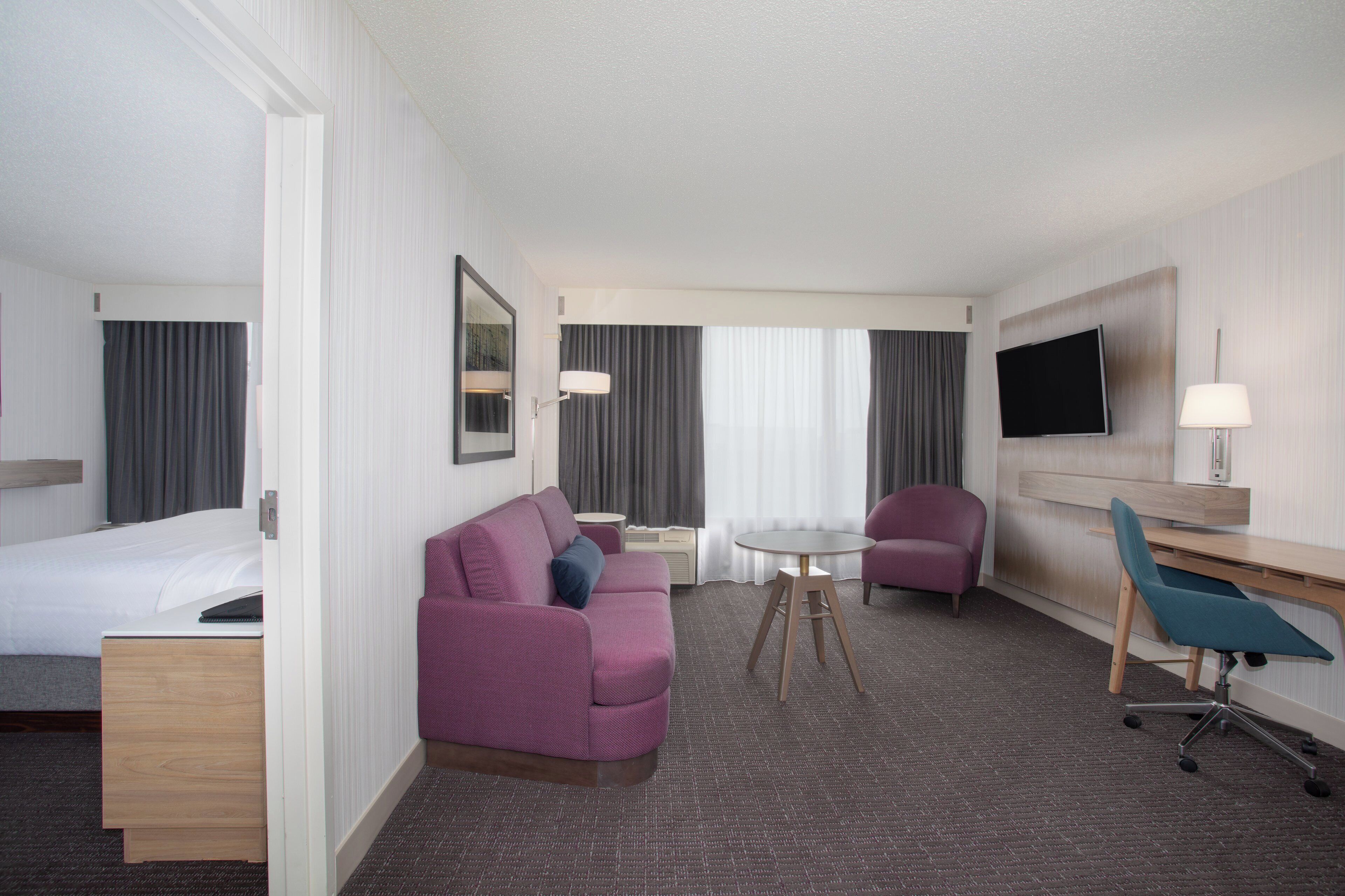 A hotel room with a bed, a sofa, a desk with a chair, a TV, and a small table.