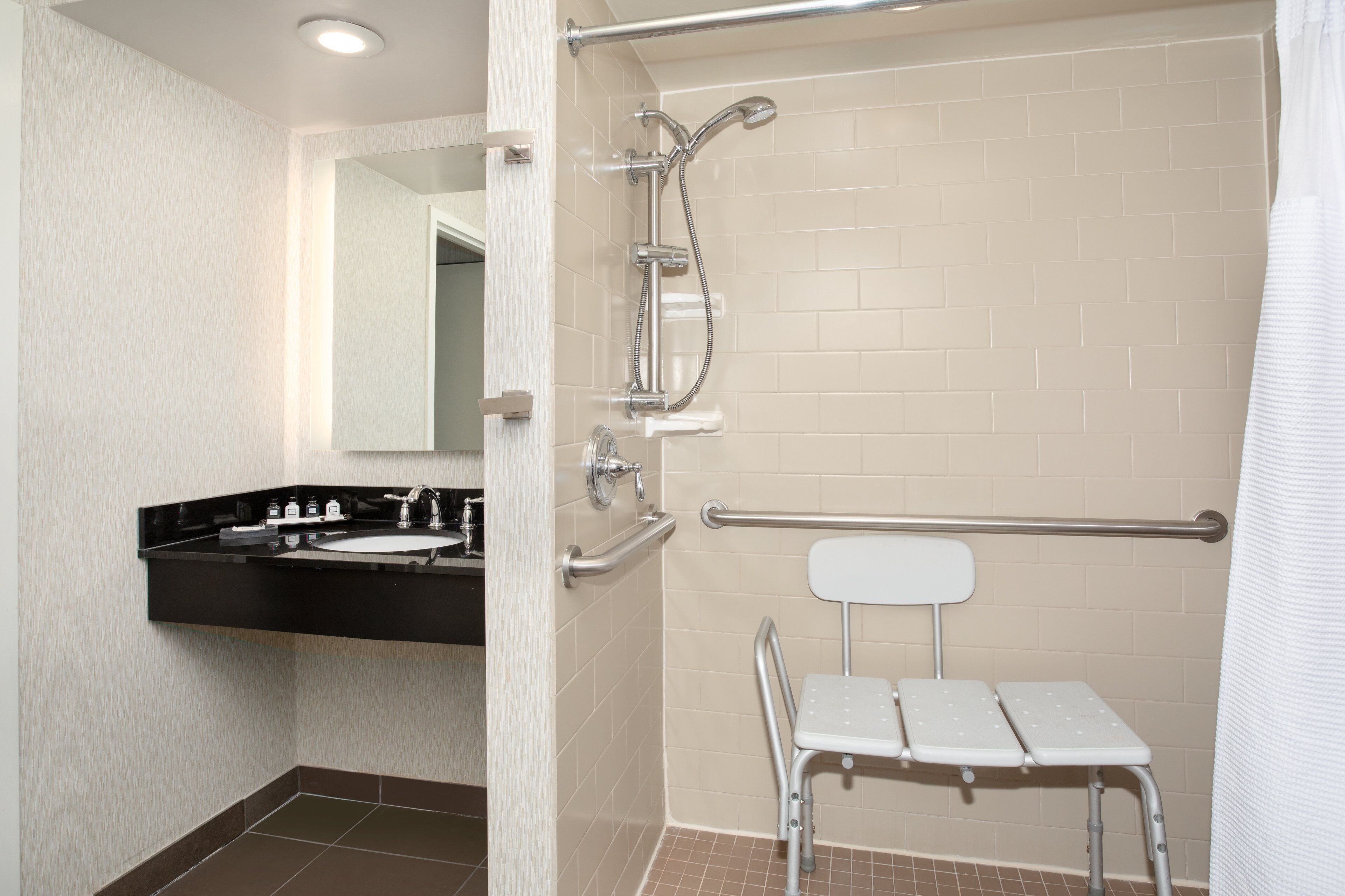 A bathroom with a black sink, a mirror, a shower with a grab bar, and a white step stool.
