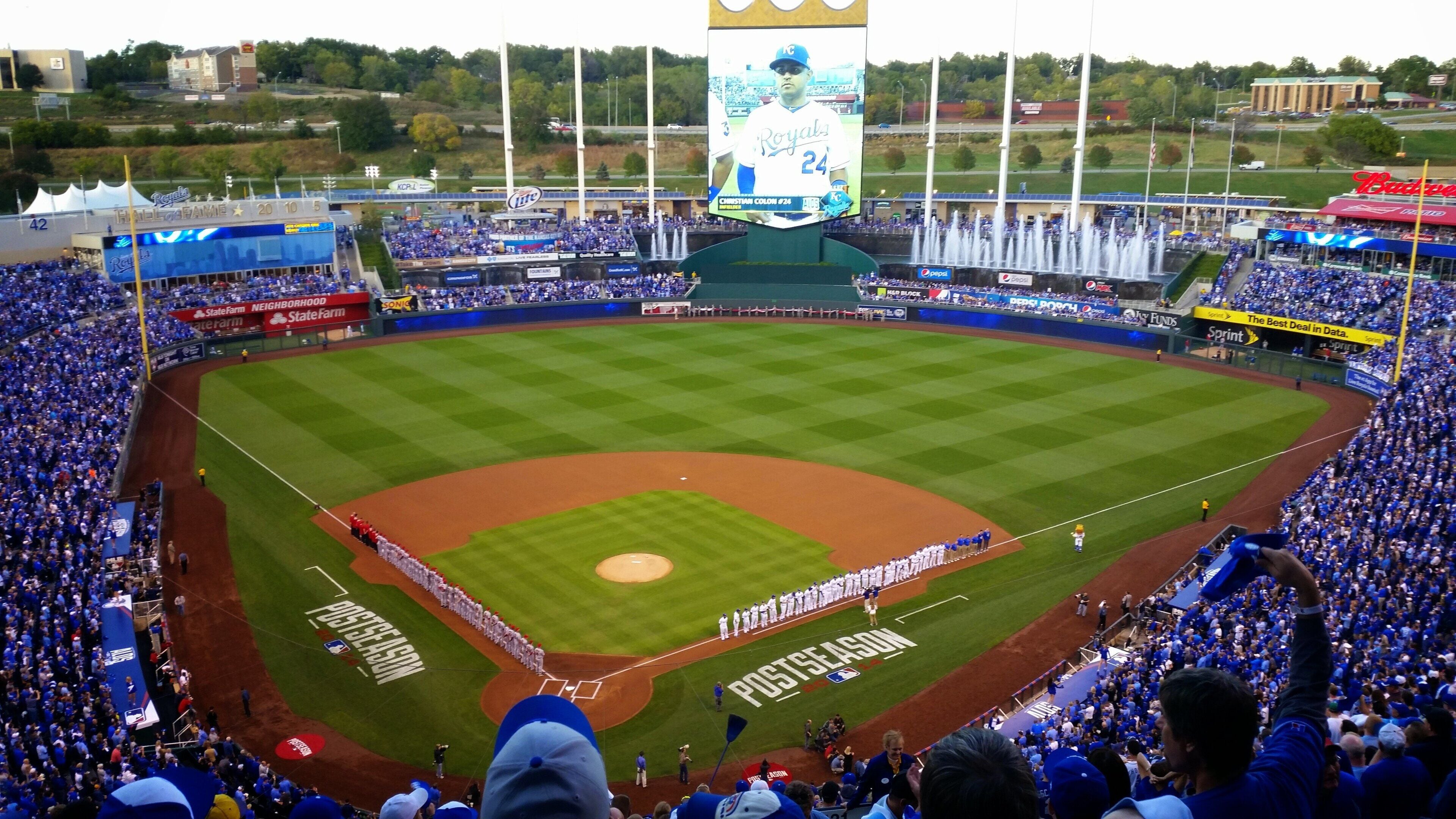 A baseball stadium with a large screen displaying a player, surrounded by spectators.
