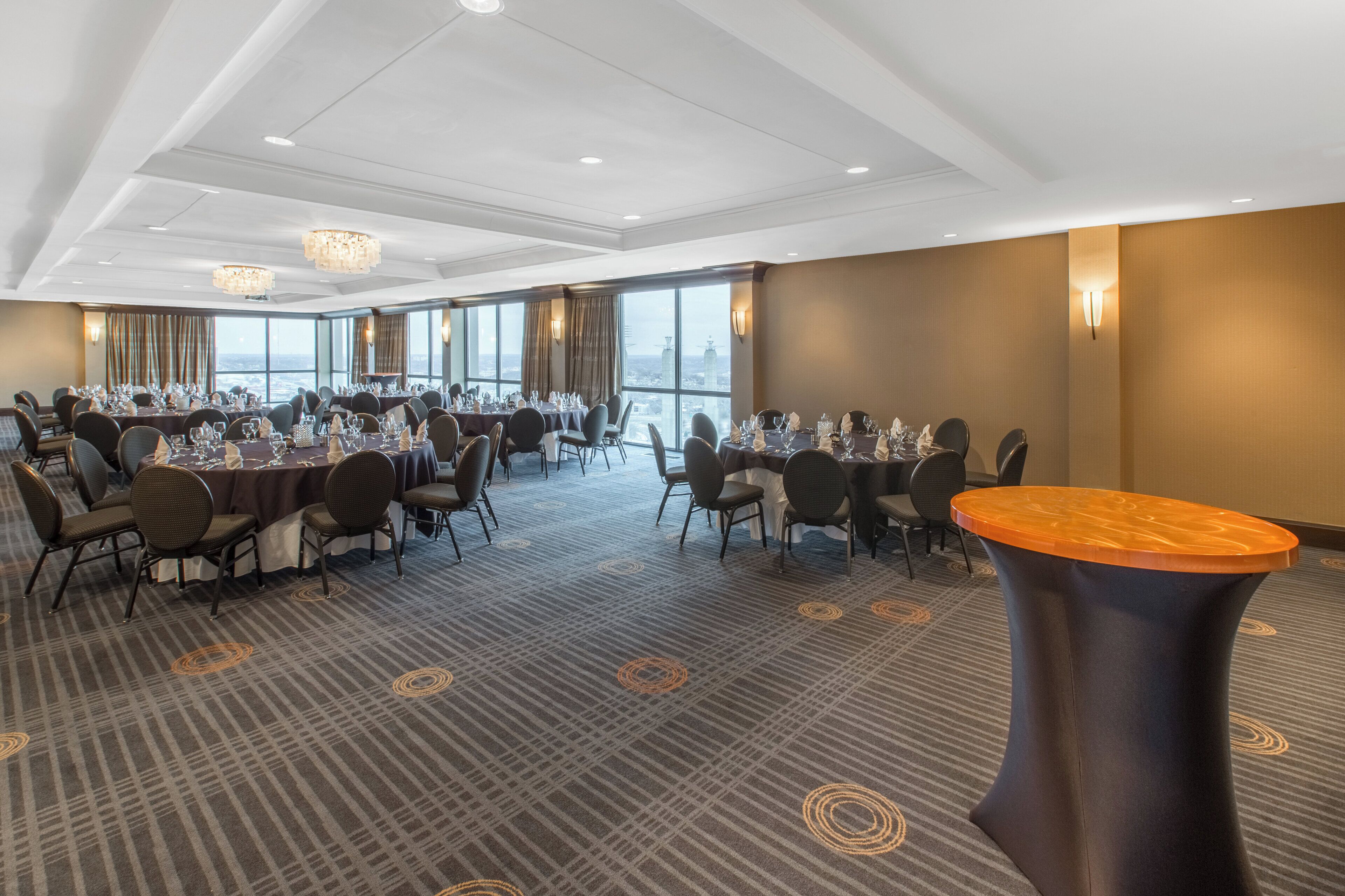 Un salón de conferencias con varias mesas dispuestas para comer, ventanas amplias y un diseño moderno en el techo.
