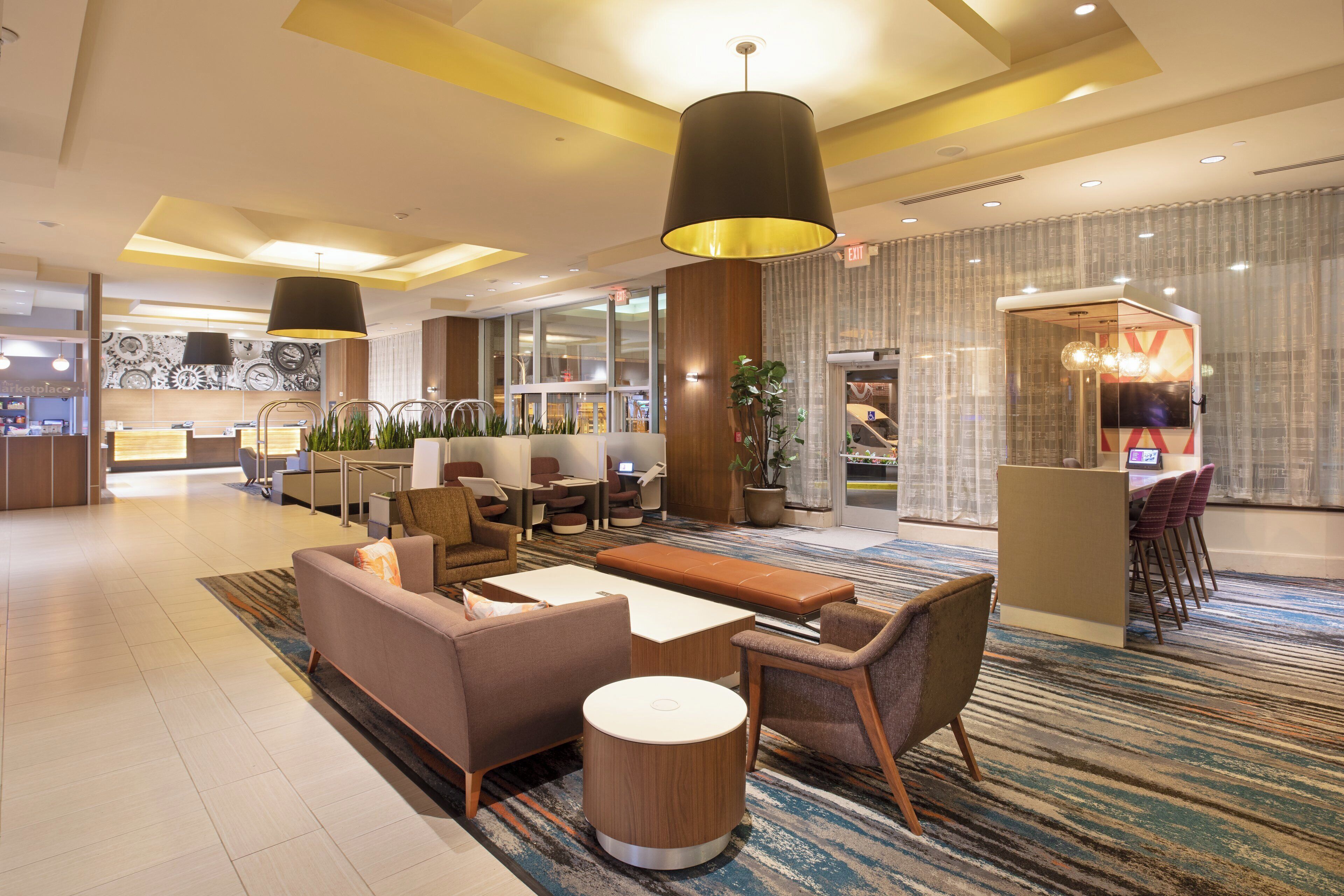 Un hall d’hôtel moderne, doté d’espaces aménagés avec des sièges, d’un comptoir de réception et offrant une vue sur l’extérieur.