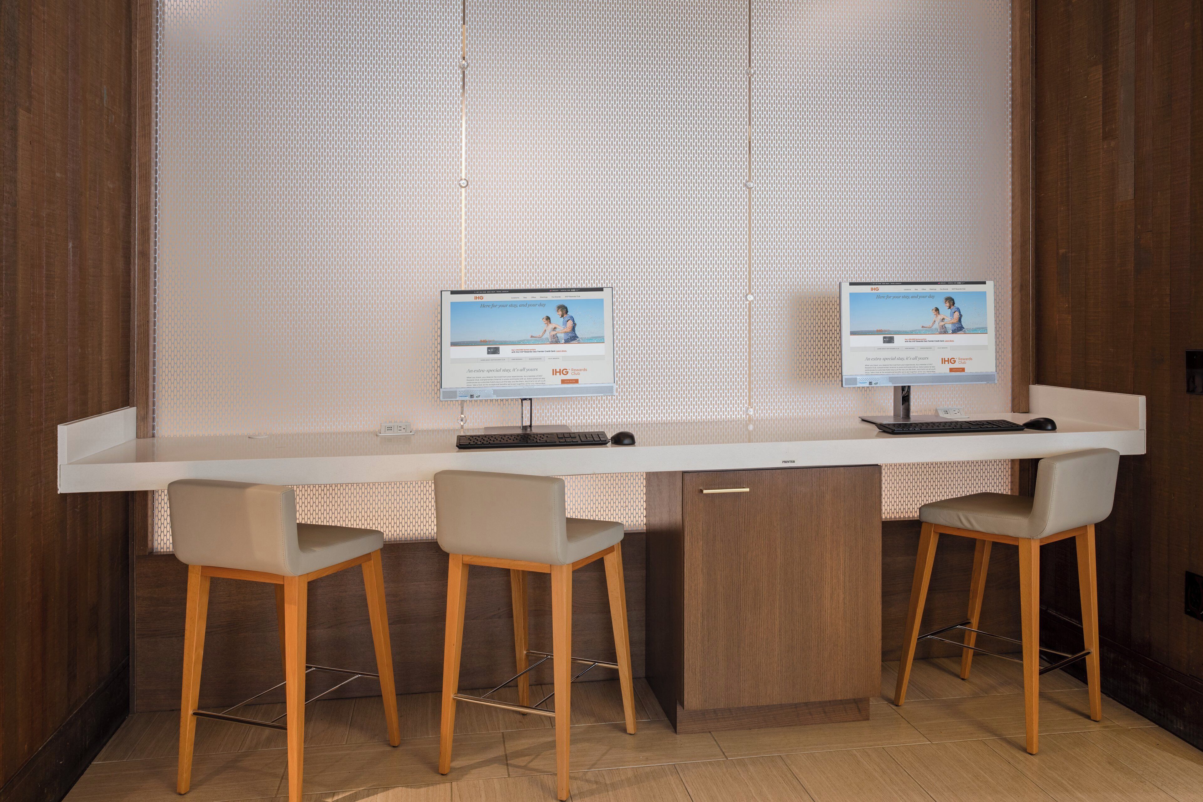 Un espace de bureau moderne comprenant deux bureaux, chacun équipé d’un ordinateur, d’un clavier et d’une souris. On y trouve trois chaises, une de chaque côté des bureaux. La pièce est dotée d’un plancher en bois et d’une grande fenêtre avec des stores.