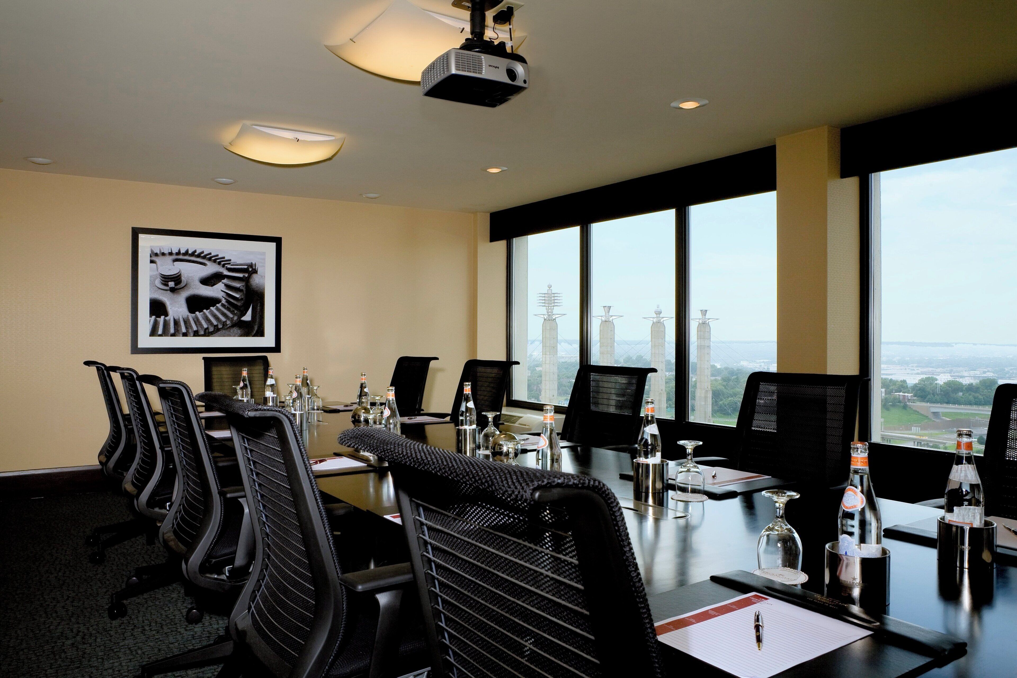 Un salón de conferencias con vistas a la ciudad, equipado con un proyector, varias sillas y mesas con botellas de agua.
